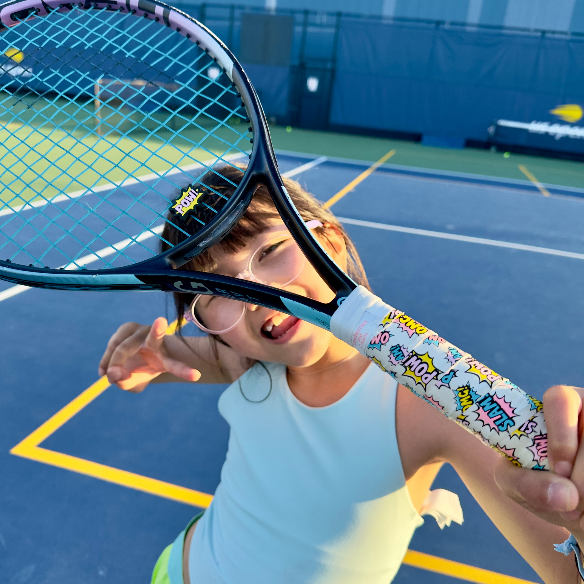 Young girl holding tennis racket adorned with Strawberries and Cream POW Collection tennis overgrip and dampener set