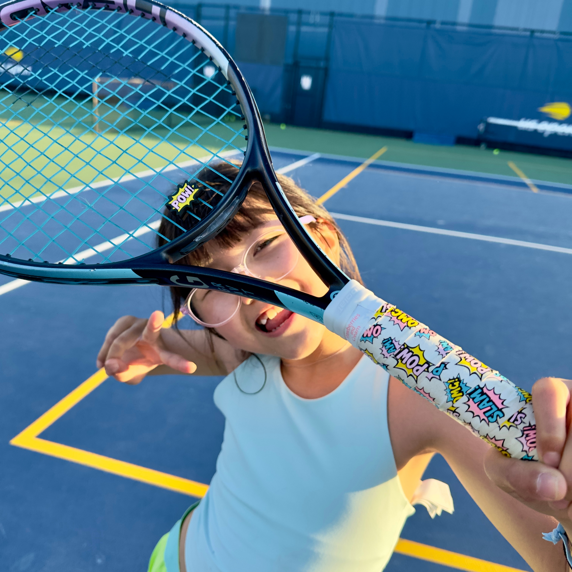 Young girl holding tennis racket adorned with Strawberries and Cream POW Collection tennis overgrip and dampener set 