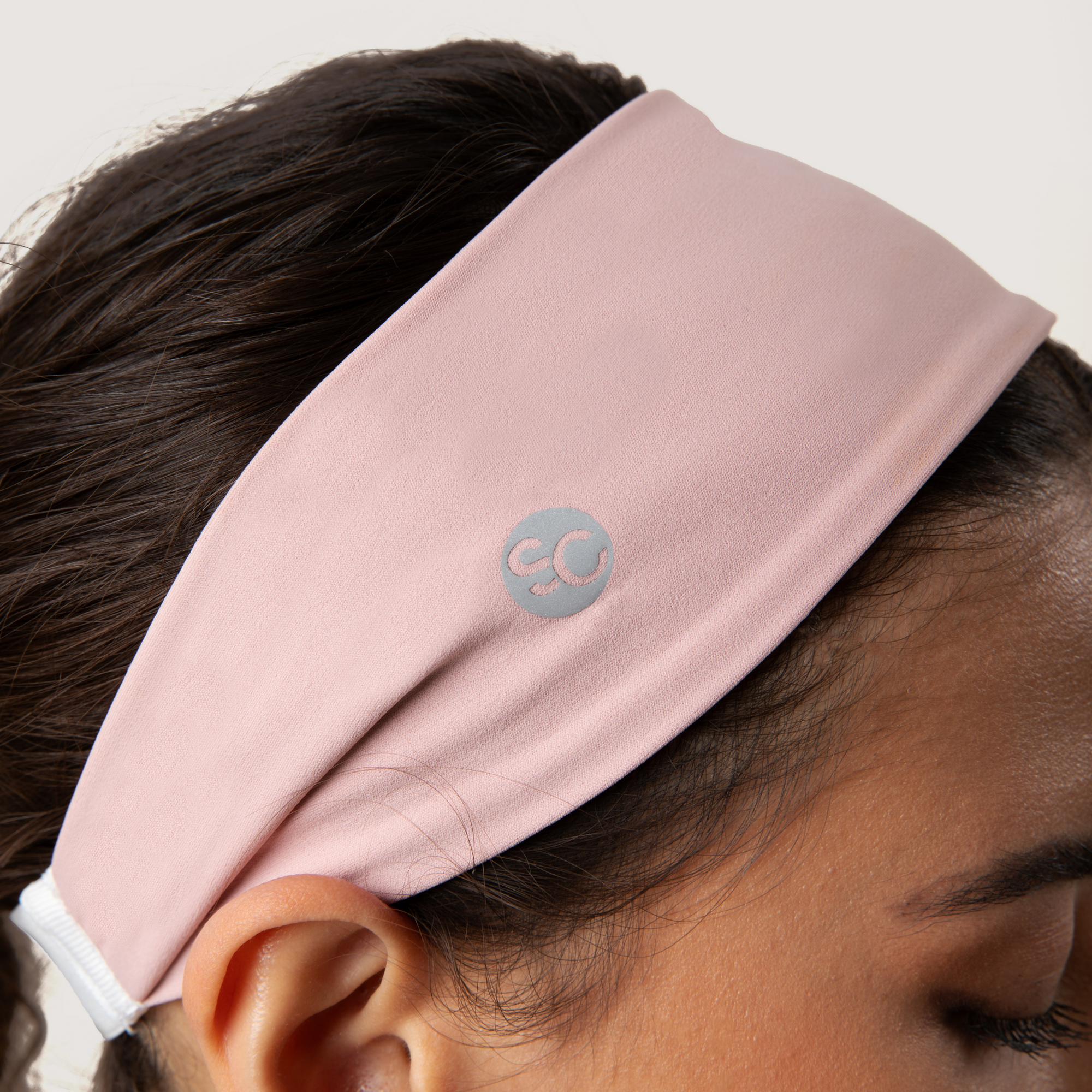 Pink headband with a reflective logo worn by a person on a neutral background