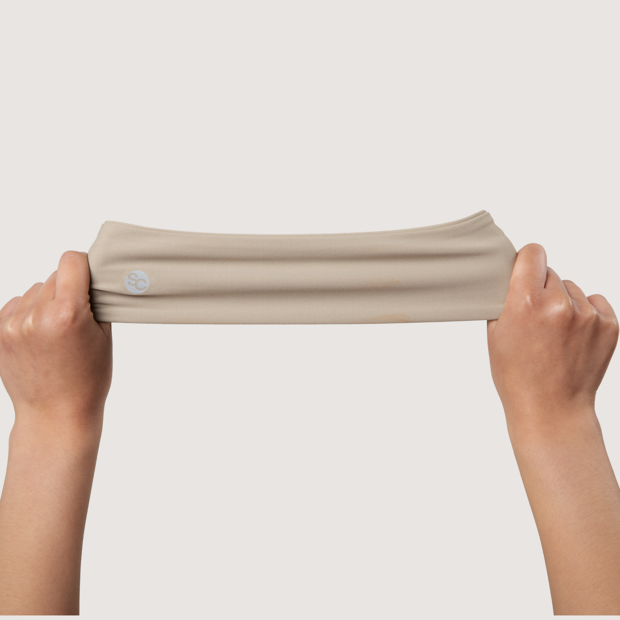 Beige headband held by hands against a plain background