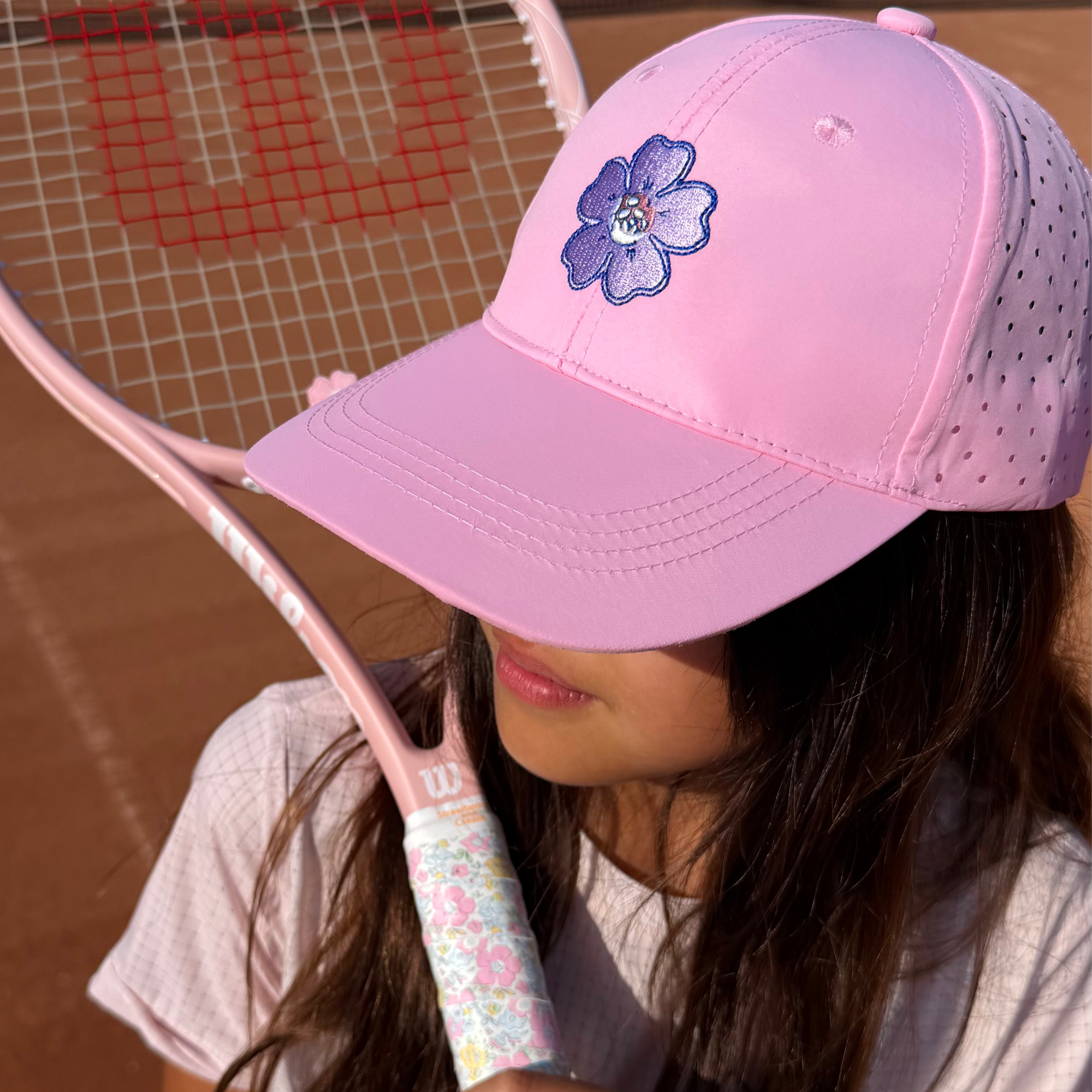 Junior player wearing Strawberries & Cream pink floral tennis trucker hat on court
